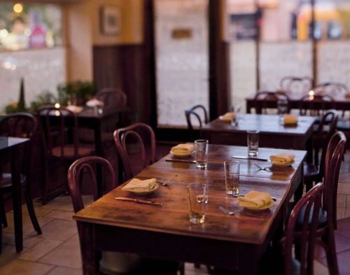 Cozy restaurant interior with wooden tables, empty chairs, and soft lighting, creating an inviting atmosphere.