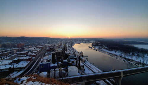 A scenic view of a river at sunset, with a city skyline and snow-covered landscape in the foreground.