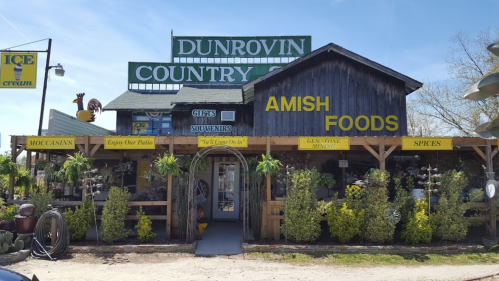 A rustic store front with signs for "Dunrovin Country," "Amish Foods," and various gifts, surrounded by decorative items.