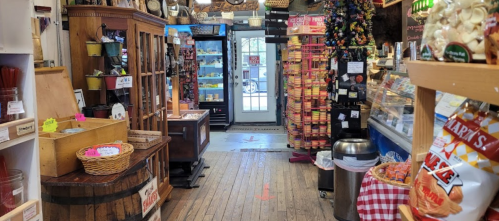 A cozy store interior with wooden floors, shelves of snacks, and a welcoming entrance. Brightly colored displays line the walls.