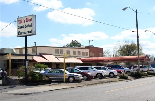 Exterior of Nikki's West Seafood Restaurant, featuring a sign and parked cars under a blue sky with clouds.