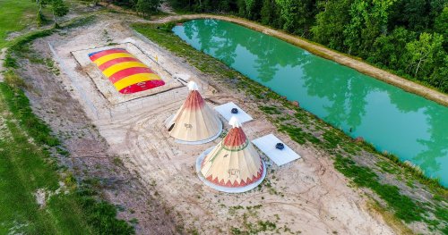 Aerial view of two teepee structures near a colorful inflatable and a pond surrounded by greenery.
