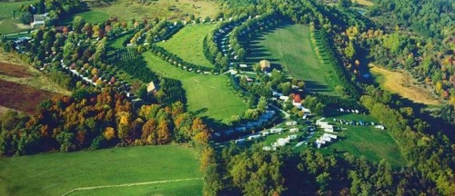 Aerial view of a lush green landscape with rows of trees, fields, and clusters of buildings in a scenic setting.