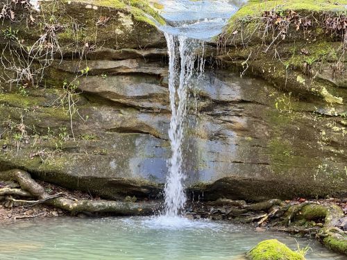 A small waterfall cascades over moss-covered rocks into a tranquil pool below.