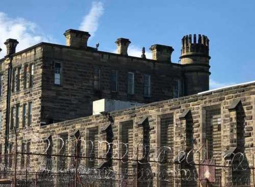 Historic stone prison building with barbed wire and a blue sky in the background.