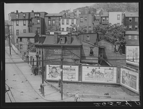 Black and white photo of a street scene with old buildings and advertisements, showcasing urban architecture and signage.