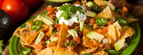A vibrant plate of nachos topped with cheese, tomatoes, jalapeños, avocado, cilantro, and sour cream.