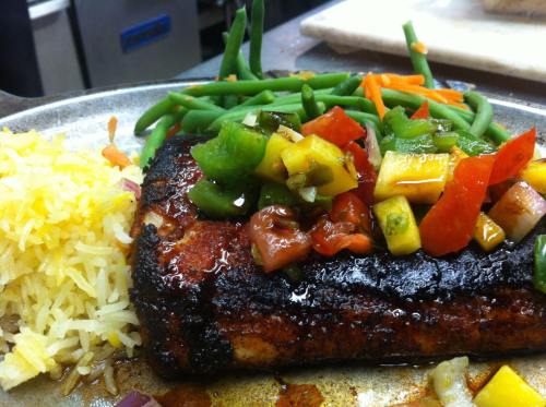 A plate of grilled salmon topped with colorful salsa, served with green beans and yellow rice.