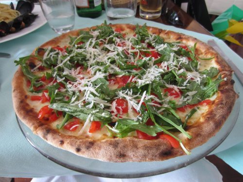 A freshly baked pizza topped with arugula, cherry tomatoes, and grated cheese on a wooden table.