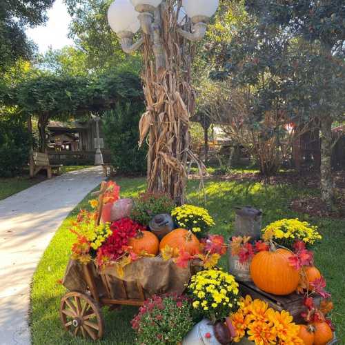 A decorative cart filled with pumpkins, flowers, and autumn leaves, set in a lush garden with a pathway.