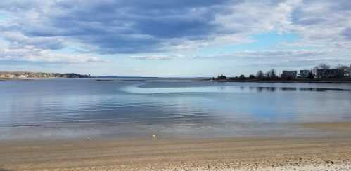 A serene beach scene with calm water, gentle waves, and a cloudy sky reflecting over the horizon.