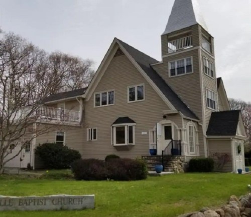 A large, modern church building with a tall steeple, surrounded by greenery and a sign that reads "Baptist Church."