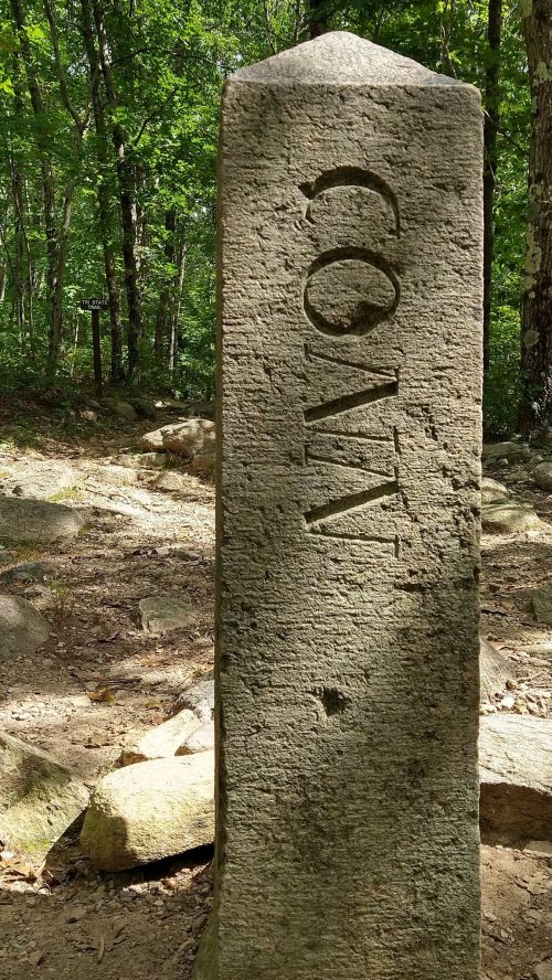 A weathered stone marker with the word "CONN" carved into it, surrounded by trees and rocky terrain.