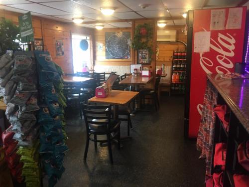 Cozy restaurant interior with wooden walls, tables, and a snack display, featuring soda machines and a relaxed atmosphere.