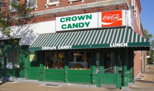 Exterior of Crown Candy, a vintage candy shop with a green awning and Coca-Cola sign, featuring colorful displays in the windows.