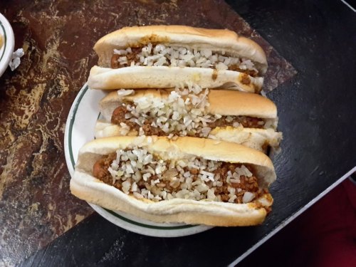 Three hot dogs in buns, generously topped with chopped onions, served on a plate.