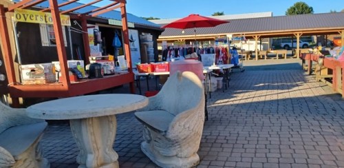 A marketplace with vendor stalls, tables, and an umbrella, showcasing various goods and clothing for sale.