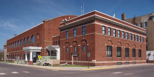 Historic brick building with large windows, located at a street corner under a clear blue sky.