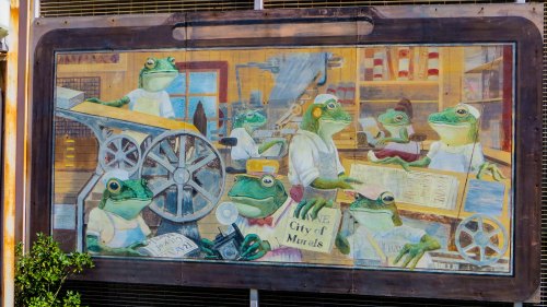 A colorful mural depicting frogs engaged in various activities in a workshop setting, showcasing a whimsical scene.