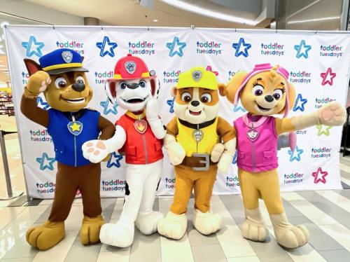Four cartoon dog characters in costumes pose together in front of a "Toddler Tuesdays" backdrop.
