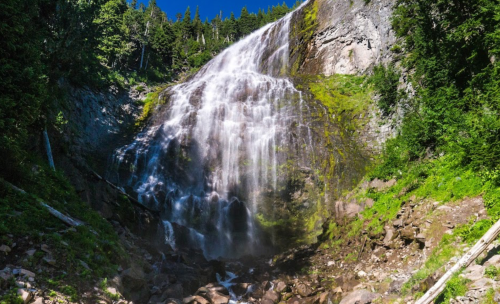 A stunning waterfall cascading down rocky cliffs, surrounded by lush greenery and bright blue skies.