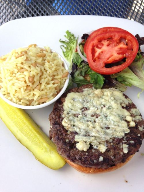 A plate featuring a blue cheese burger, rice, salad with tomato, and a pickle on the side.