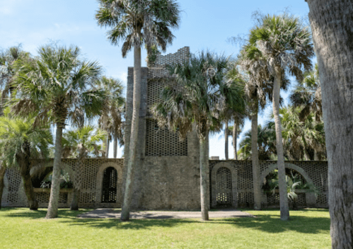 A stone structure surrounded by palm trees under a clear blue sky.