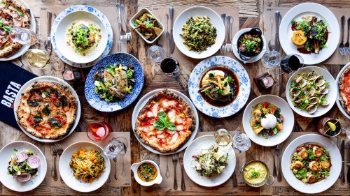 A vibrant spread of various dishes, including pizza, pasta, salads, and appetizers, arranged on a wooden table.