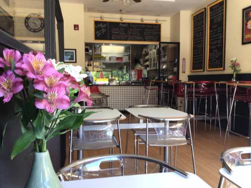 A cozy café interior with clear tables, red stools, a flower vase, and a chalkboard menu in the background.