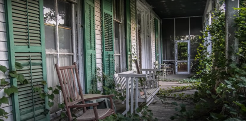 Abandoned porch with green shutters, rocking chairs, and overgrown ivy, creating a hauntingly serene atmosphere.