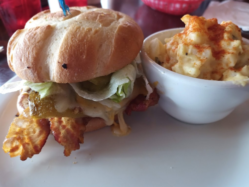 A sandwich with bacon, lettuce, and cheese, served with a side of creamy potato salad in a white bowl.