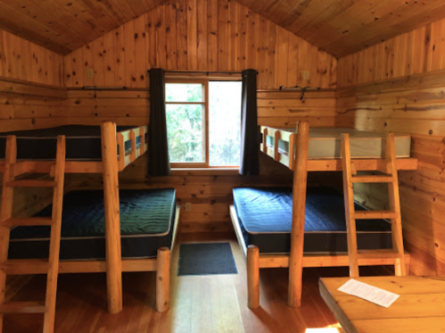 Cozy cabin interior with two wooden bunk beds and a window, featuring wooden walls and a warm, rustic atmosphere.