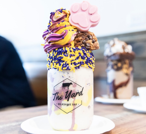 A colorful milkshake topped with whipped cream, sprinkles, cookies, and a pink paw-shaped candy in a branded jar.