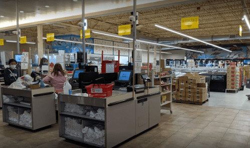 A grocery store checkout area with cash registers, shoppers, and shelves in the background.