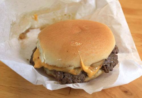 A cheeseburger with melted cheese and a beef patty, wrapped in white paper on a wooden surface.