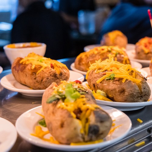Baked potatoes topped with cheese, green onions, and chili, served on white plates in a restaurant setting.