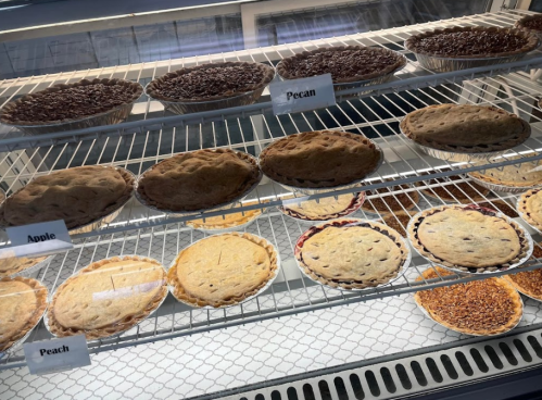 A display case filled with various pies, including pecan, apple, and peach, on multiple shelves.
