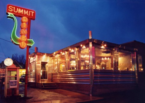 A retro diner with neon signage, glowing lights, and a shiny exterior, set against a twilight sky.