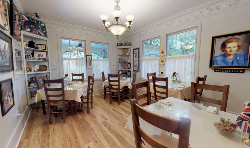 Cozy restaurant interior with wooden tables, chairs, and decor featuring artwork and a portrait on the wall.