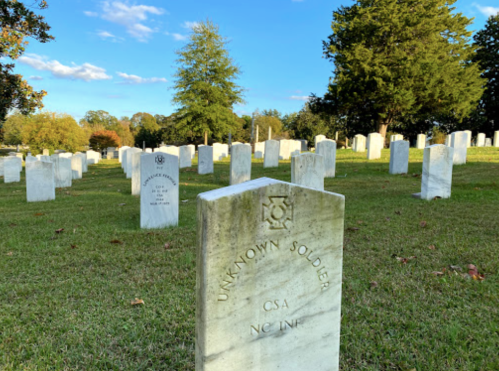 Gravestones in a cemetery, with a prominent marker for "Unknown Soldier, CSA, NC Inf" under a clear blue sky.