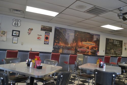 Retro diner interior with checkered floor, red stools, and vintage wall art depicting a city scene.