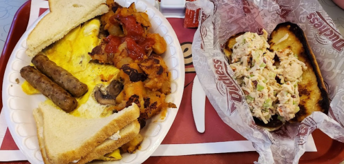 A plate with scrambled eggs, sausage, hash browns, toast, and a sandwich filled with chicken salad.