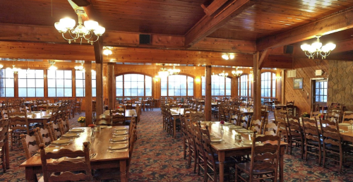 A spacious wooden dining hall with long tables, chairs, and warm lighting, featuring a cozy, rustic atmosphere.