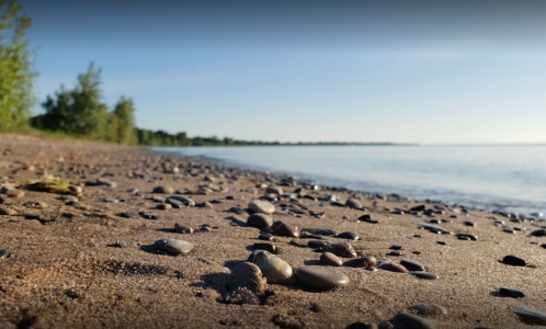 A serene beach scene with smooth pebbles on the sand, gentle waves lapping at the shore under a clear blue sky.