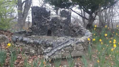A stone structure resembling a small castle, surrounded by blooming daffodils and trees in a garden setting.