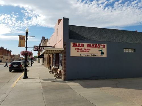 A street view featuring Mad Mary's Steak House & Saloon with a blue sky and nearby storefronts.