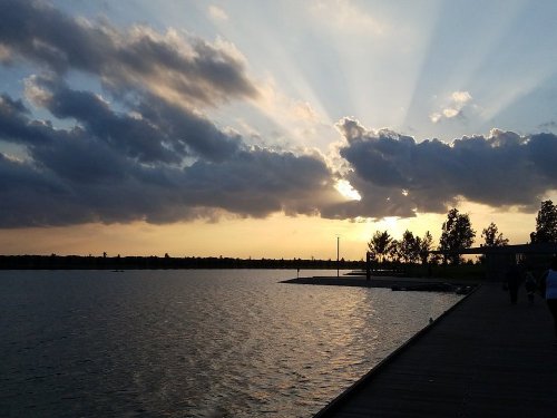 A serene lakeside view at sunset, with rays of light breaking through clouds and reflecting on the water.