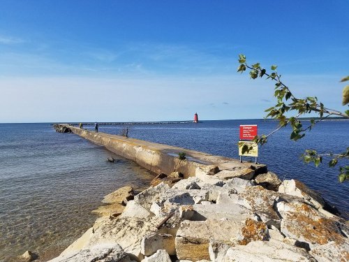A long pier extends into calm waters, with a red lighthouse in the distance under a clear blue sky.