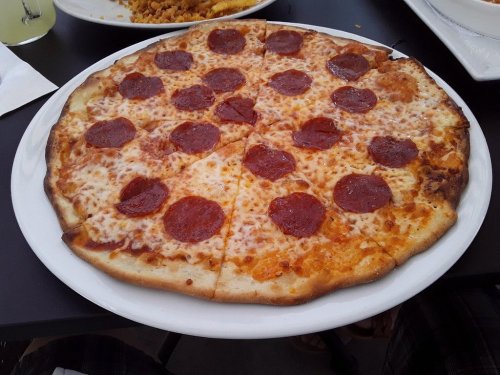 A large pizza topped with pepperoni slices and melted cheese on a white plate.