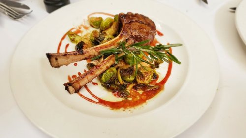 A plate featuring grilled lamb chops, Brussels sprouts, and a drizzle of sauce, garnished with a sprig of rosemary.